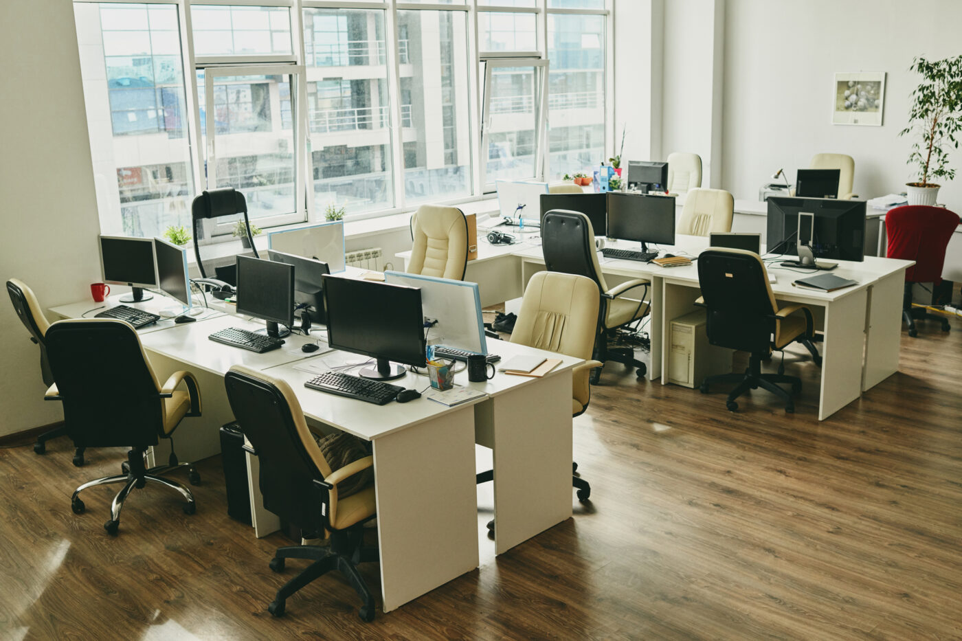 Modern office with big window and desks with computers and mugs.